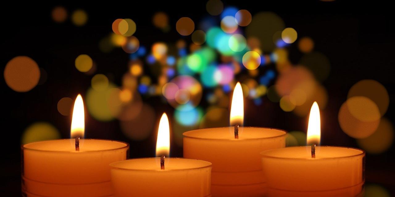 4 orangene, brennende Kerzen vor einem glitzernden, unscharf gehaltenen Hintergrund