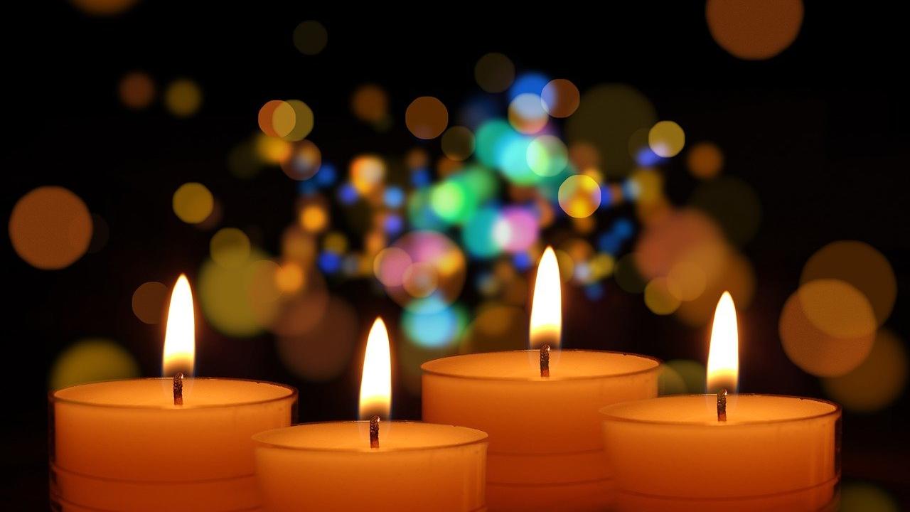 4 orangene, brennende Kerzen vor einem glitzernden, unscharf gehaltenen Hintergrund