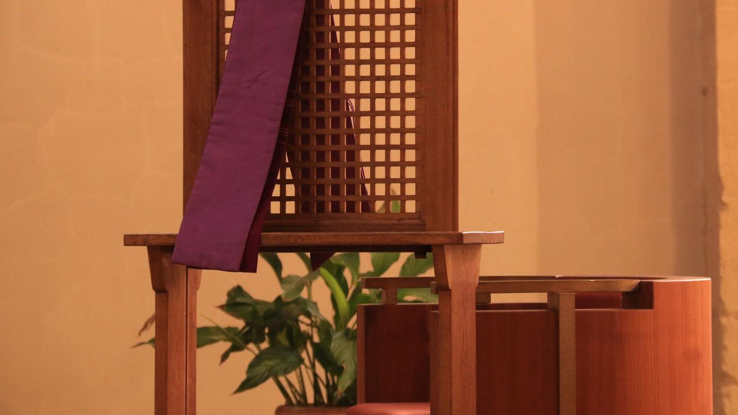 Foto eines Beichtstuhls aus Holz, über der Lehne hängt eine violette Schärpe