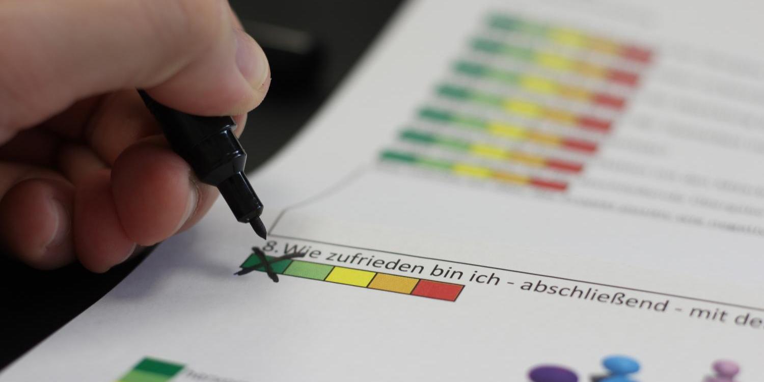Hand markiert Bewertungsskala auf einem Papier mit grünem Stift.