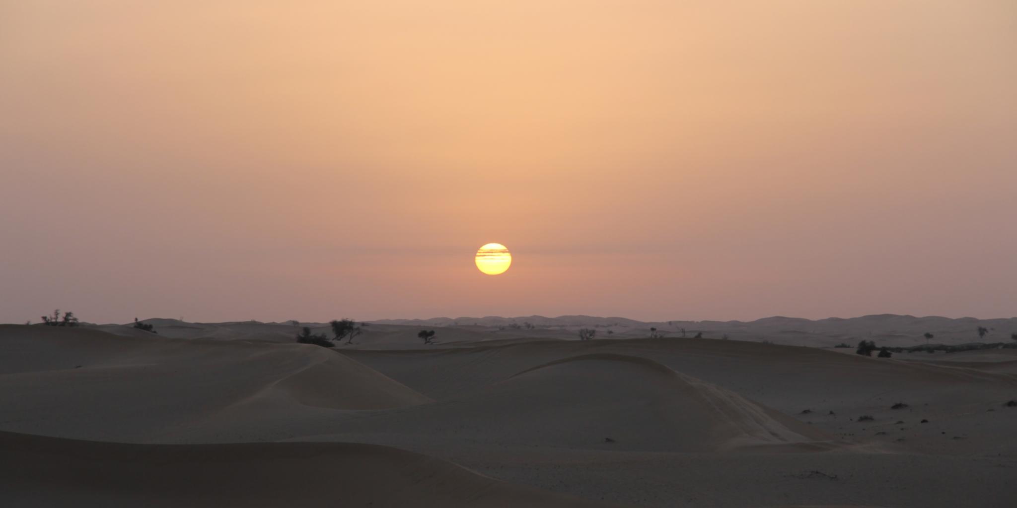 Sonnenaufgang vor einer hügeligen, kargen Landschaft im frühmorgendlichen Licht