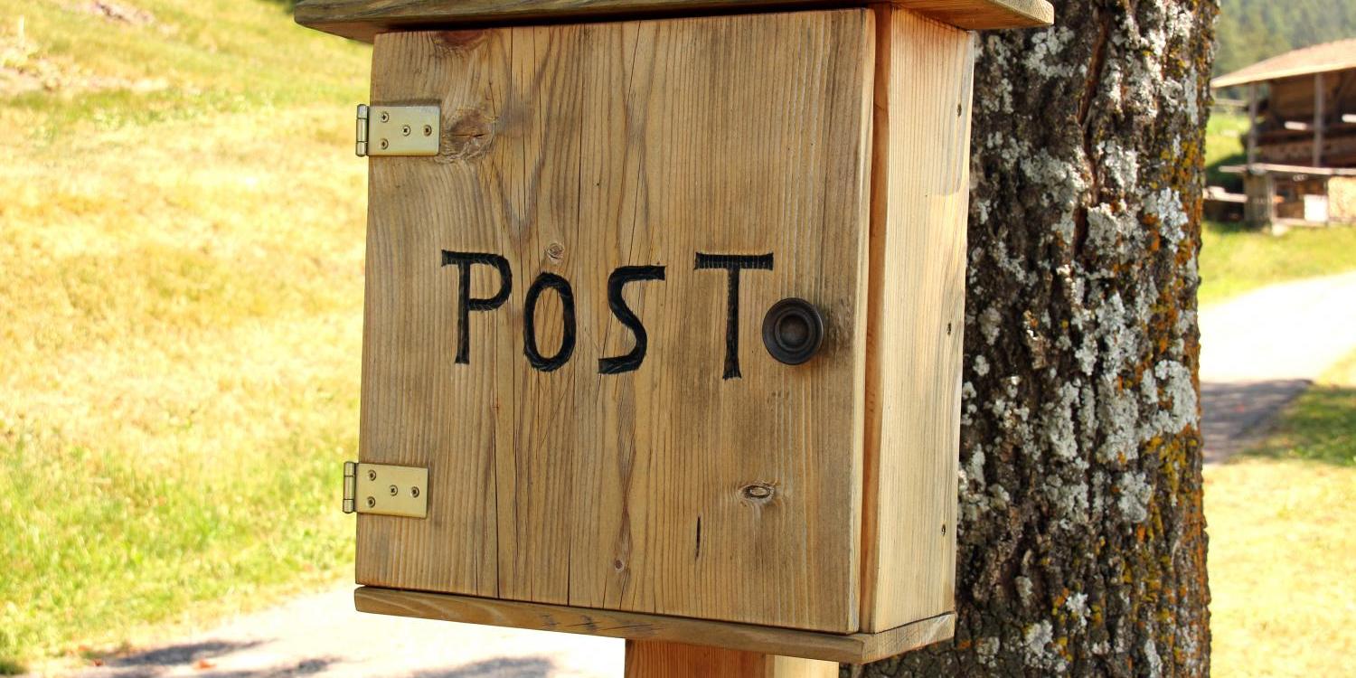 Holzbriefkasten mit der Aufschrift POST der vor einem Baumstamm befestigt ist; dahinter ist ein Feldweg an einem Berghang zu sehen (c) Bild: Peter Weidemann In: Pfarrbriefservice.de Holzbriefkasten mit der Aufschrift POST der vor einem Baumstamm befestigt ist; dahinter ist ein Feldweg an einem Berghang zu sehen
