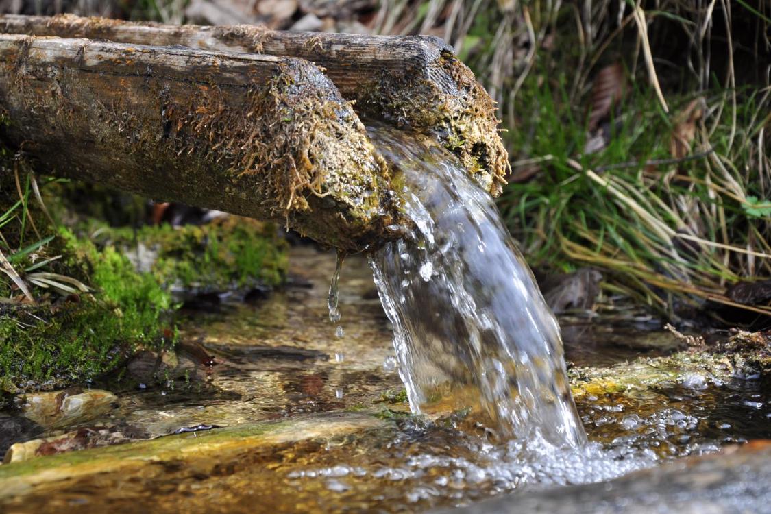 Wasser fließt aus einem Brunnenrohr in einen kleinen Teich
