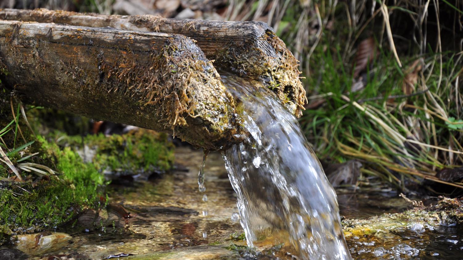 Wasser fließt aus einem Brunnenrohr in einen kleinen Teich