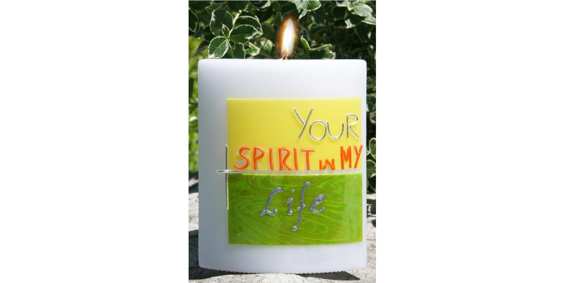 Foto einer brennenden weißen Firmkerze, die Kerze ist relativ dick und hat vorne eine gelb-grünes Logo mit der Inschrift 'Your spirit in my life'