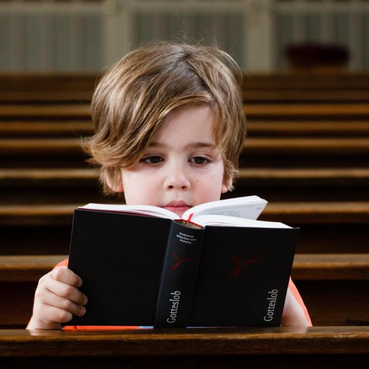 Kind mit Gebetbuch in einer Kirchenbank