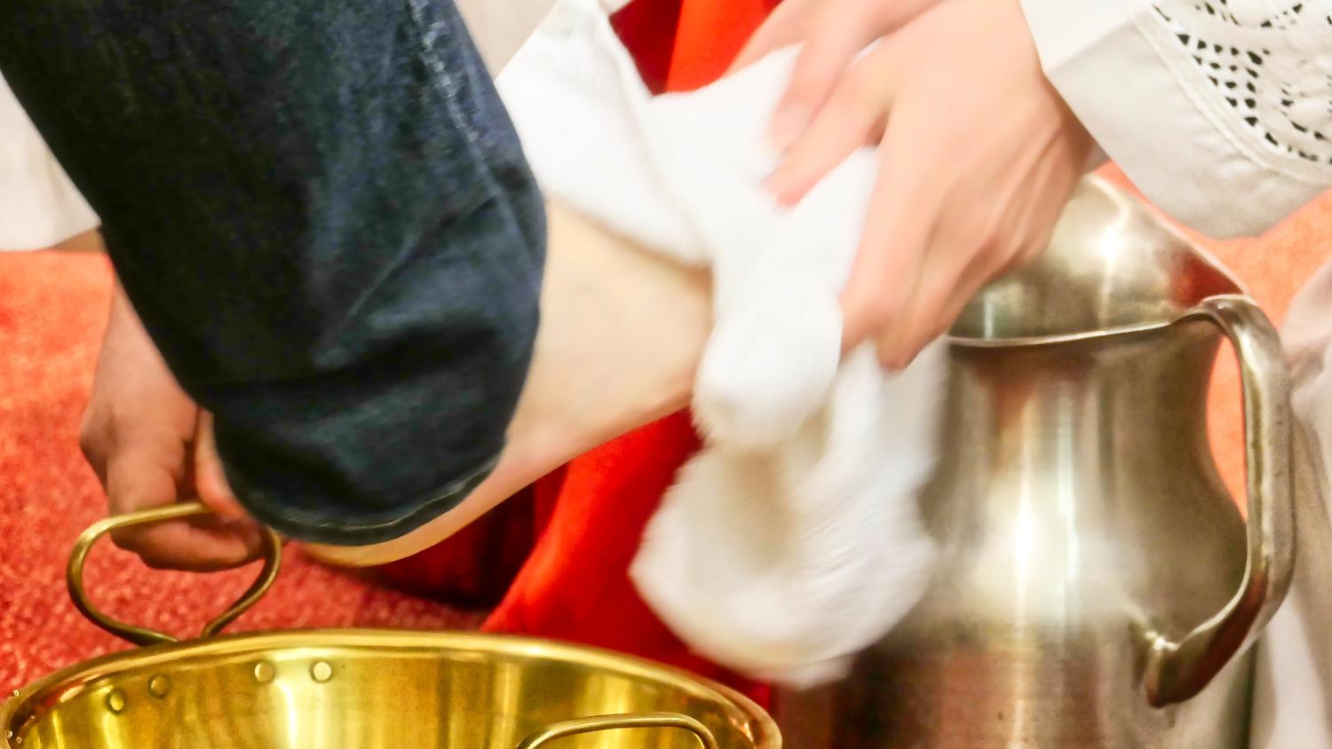 Priester wäscht einem Gläubigen die Füße, das Wasser kommt aus einem silbernen Kelch mit Henkel,