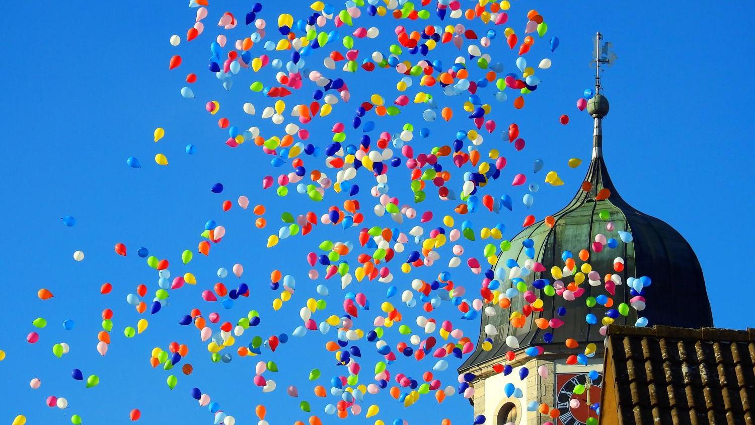 Bunte Luftballons vor der Spitze eines Kirchturms