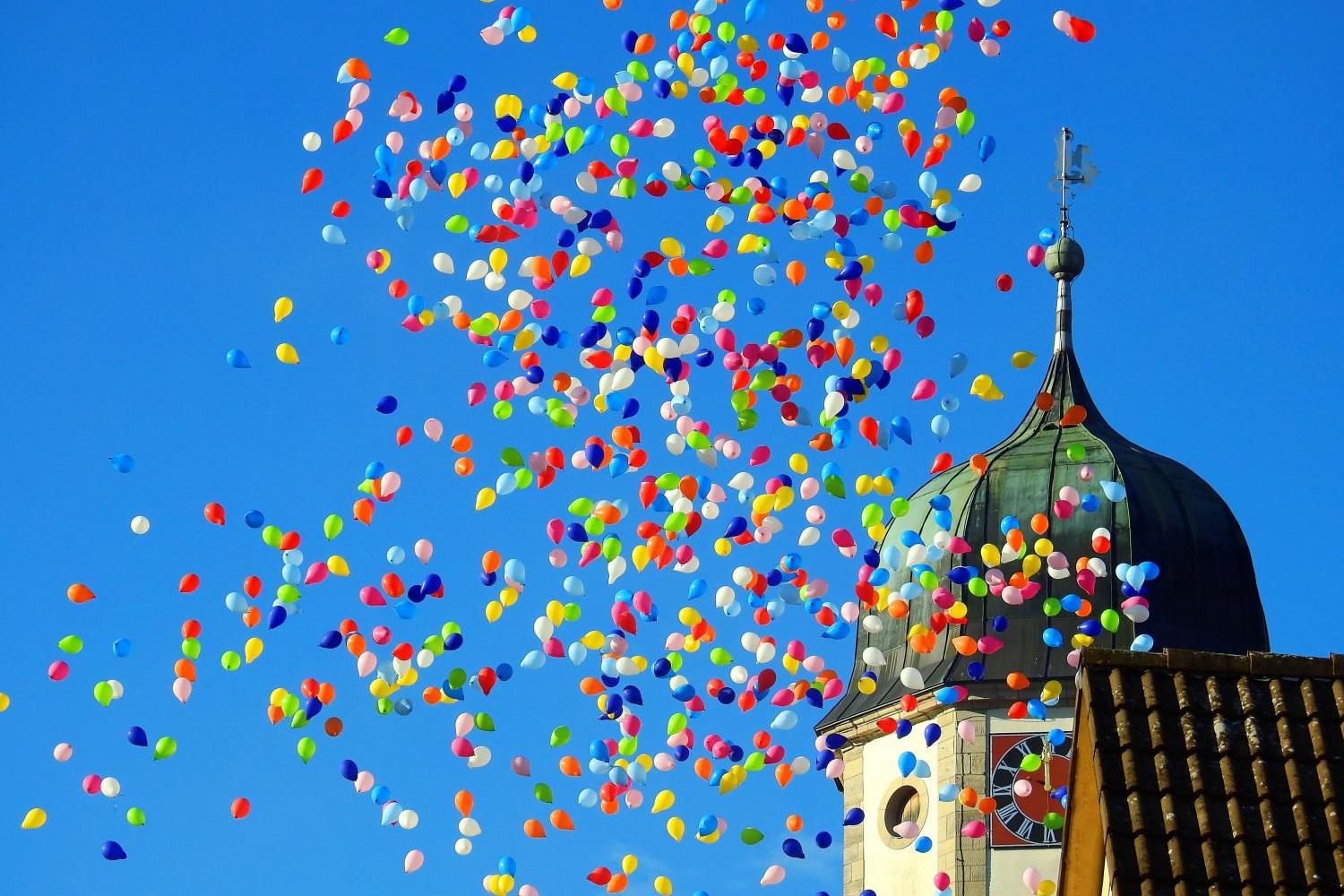 Bunte Luftballons vor der Spitze eines Kirchturms