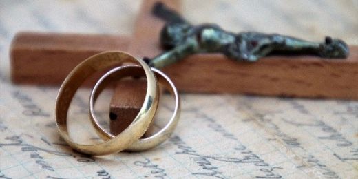 Ein Holzkreuz mit Korpus auf einem handbeschriebenen Blatt; an das Kreuz angelehnt: zwei Eheringen