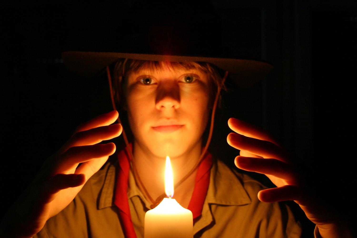 Porträt eines Pfadfinders in seiner Uniform, vor dunklem Hintergrund mit einer brennenden Kerze