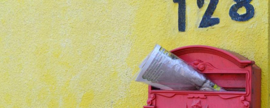 Zeitschrift steckt in einem roten, südeuropäisch anmutenden Briefkasten an gelber Hauswand