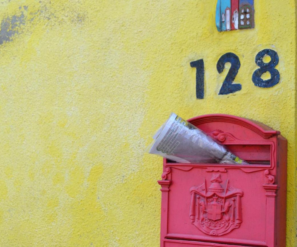 Zeitschrift steckt in einem roten, südeuropäisch anmutenden Briefkasten an gelber Hauswand