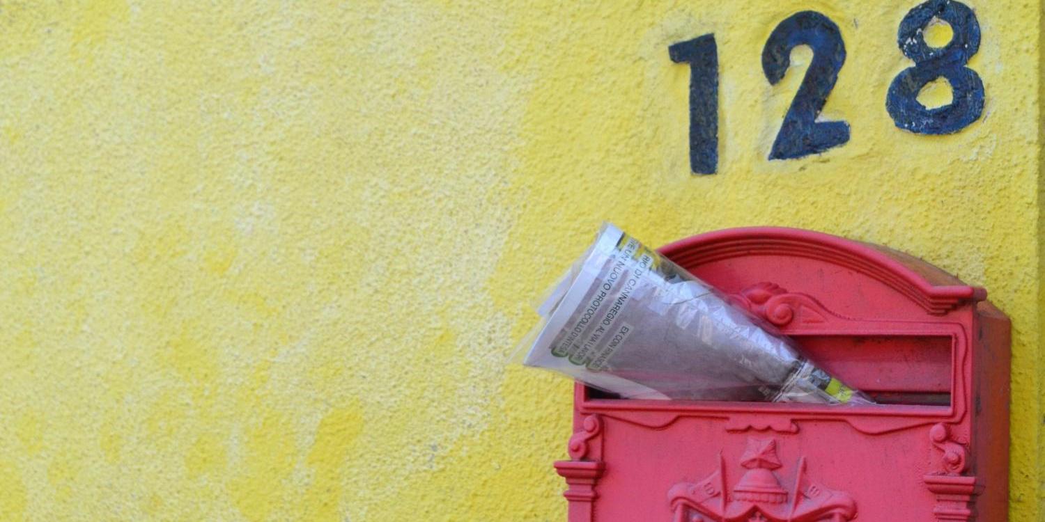 Zeitschrift steckt in einem roten, südeuropäisch anmutenden Briefkasten an gelber Hauswand (c) Bild: Monika Jesionkowska In: Pfarrbriefservice.de Zeitschrift steckt in einem roten, südeuropäisch anmutenden Briefkasten an gelber Hauswand