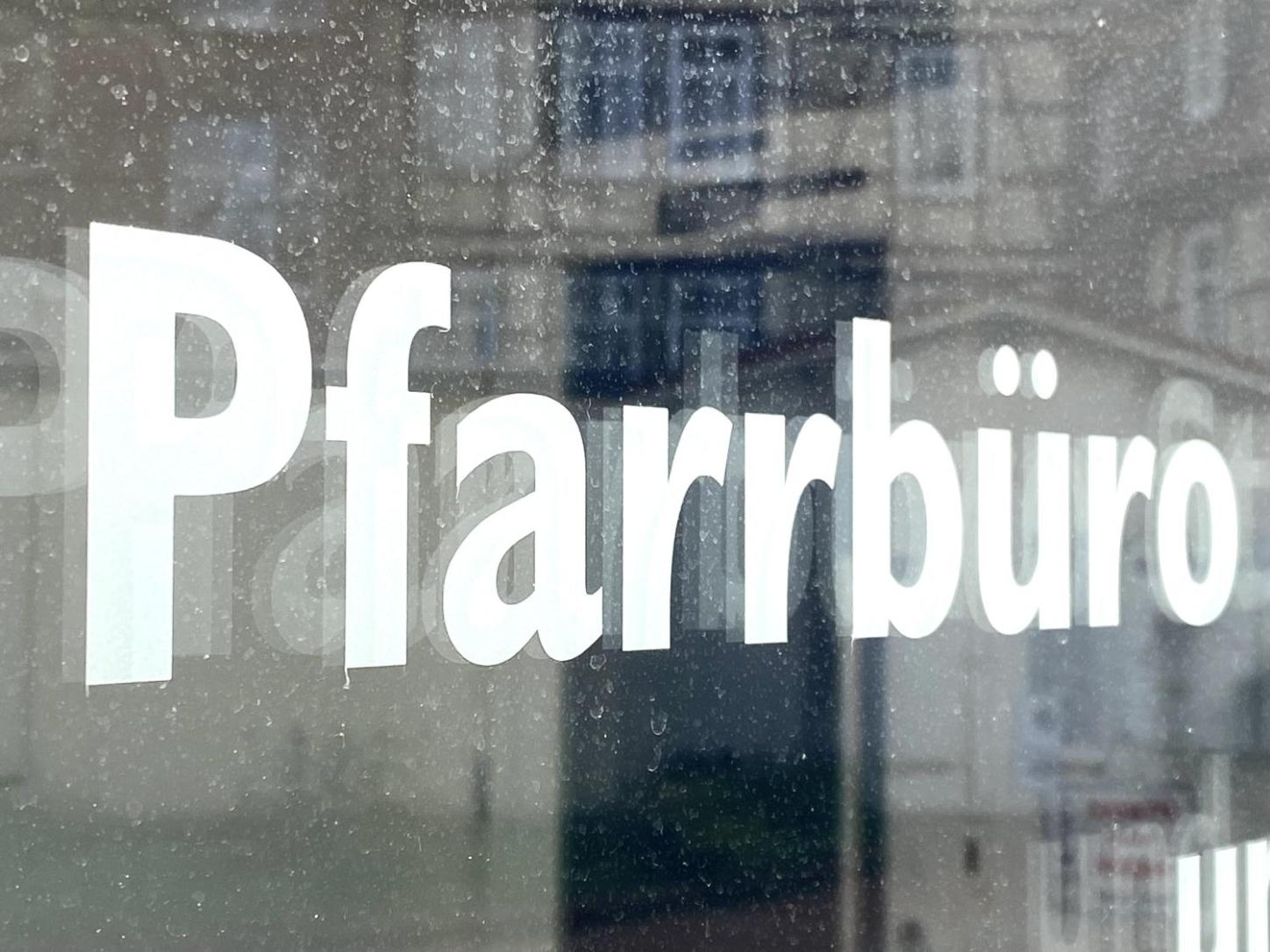 Schild mit Aufschrift 'Pfarrbüro' vor unscharfem Hintergrund