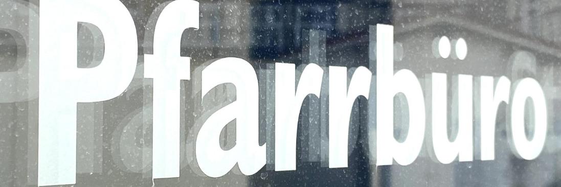 Schild mit Aufschrift 'Pfarrbüro' vor unscharfem Hintergrund