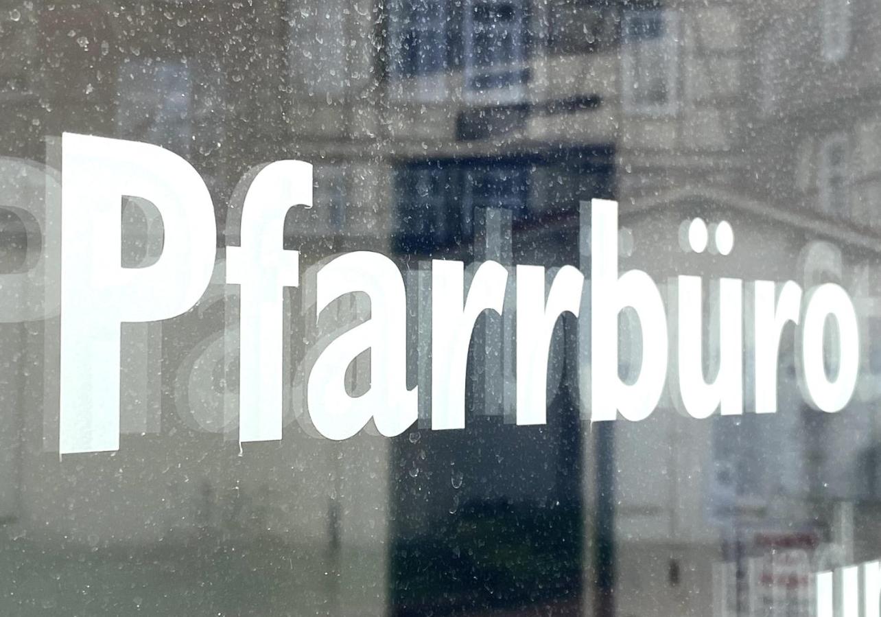Schild mit Aufschrift 'Pfarrbüro' vor unscharfem Hintergrund