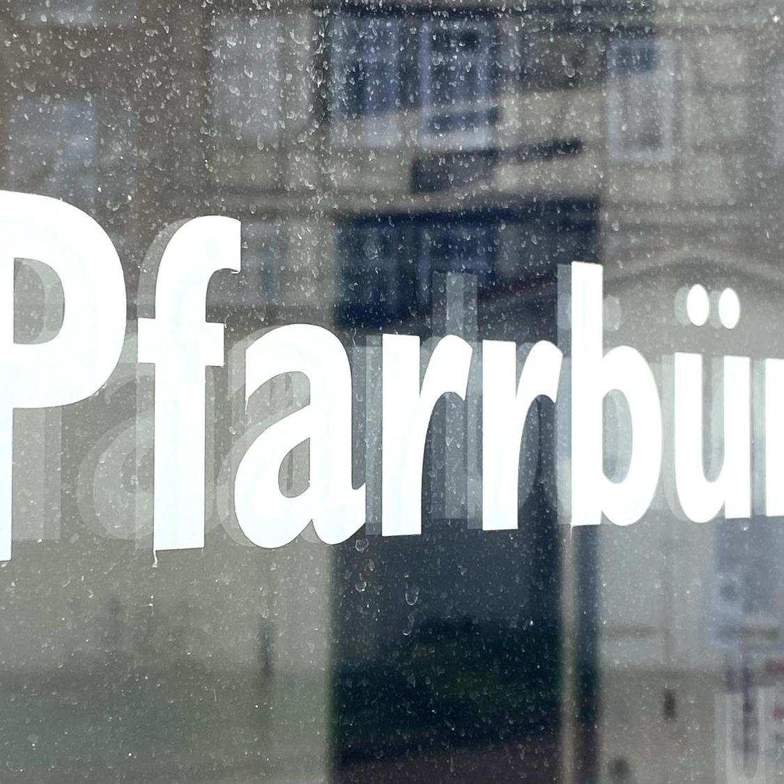 Schild mit Aufschrift 'Pfarrbüro' vor unscharfem Hintergrund
