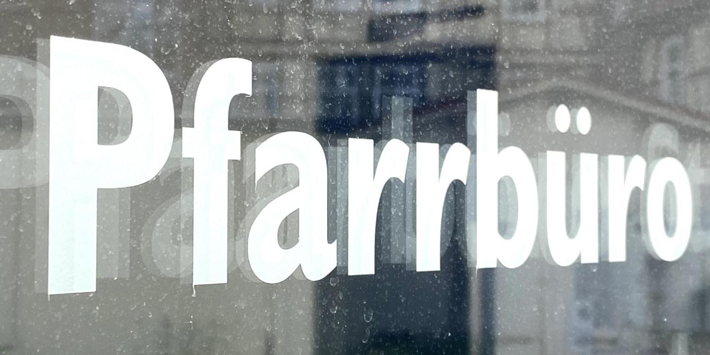 Schild mit Aufschrift 'Pfarrbüro' vor unscharfem Hintergrund