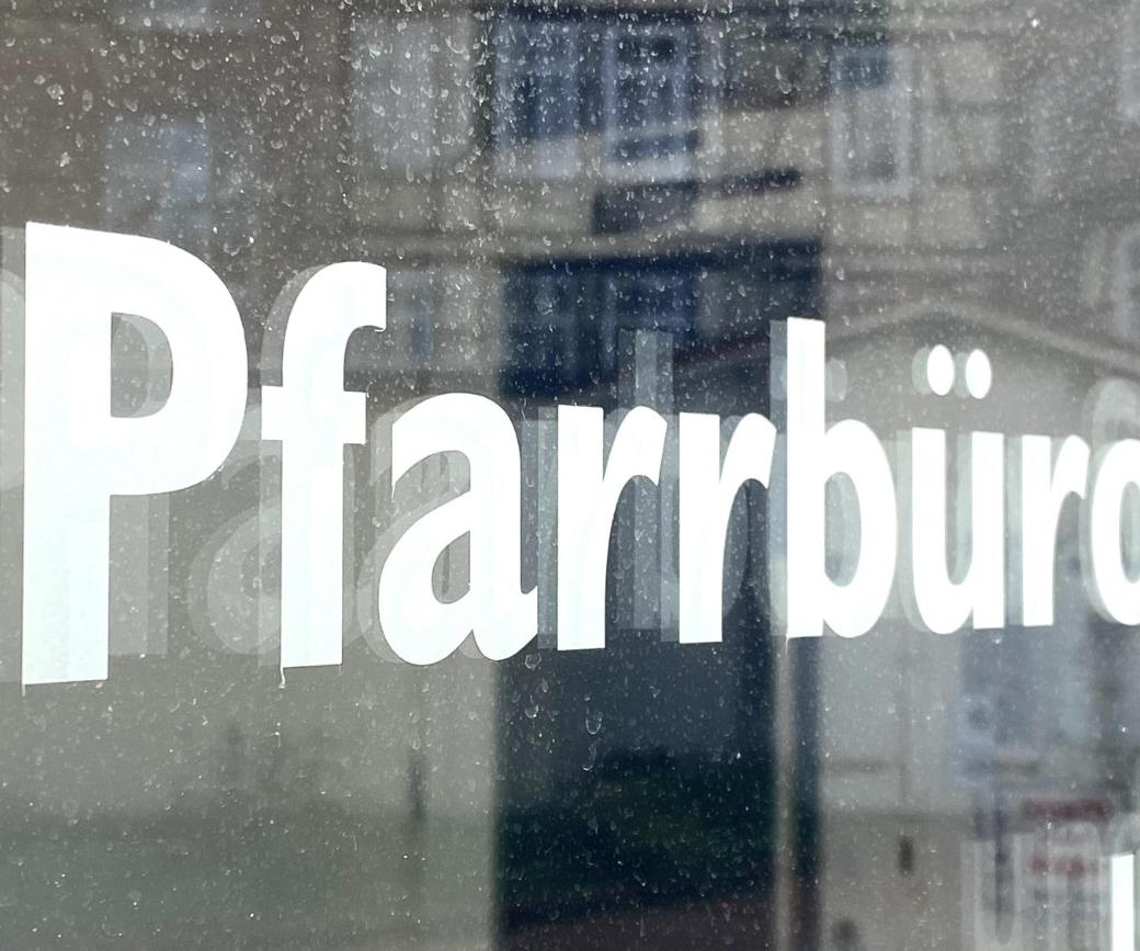 Schild mit Aufschrift 'Pfarrbüro' vor unscharfem Hintergrund