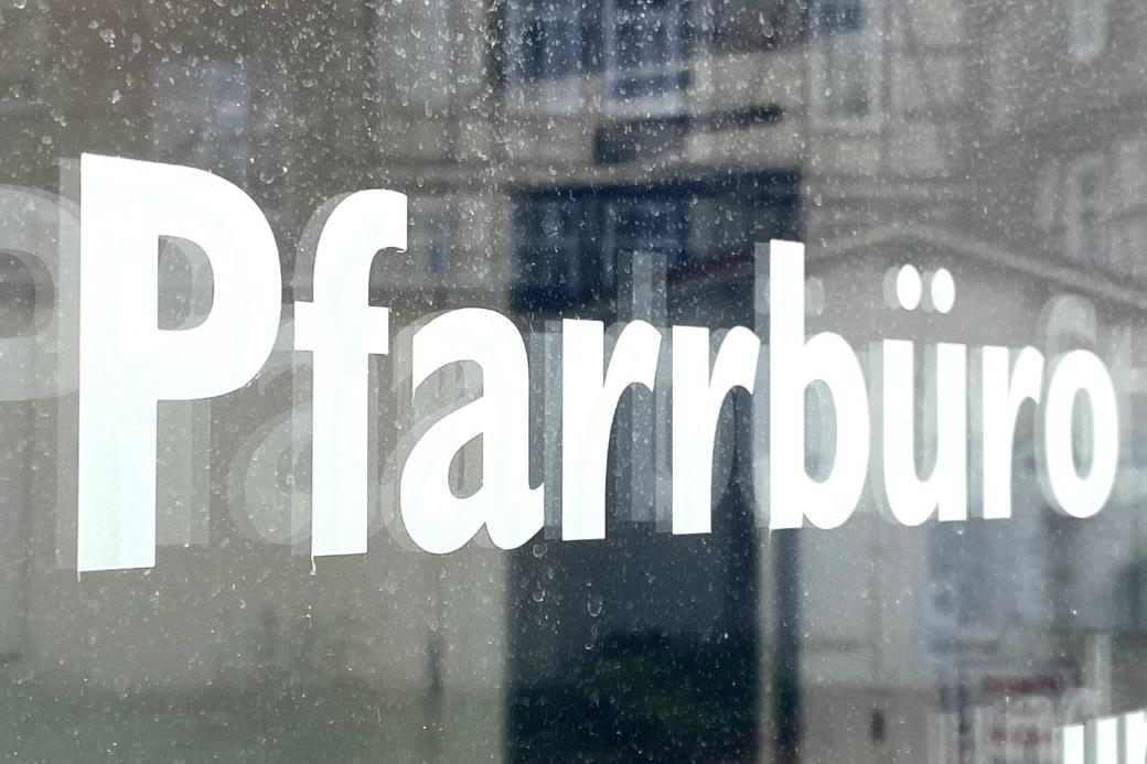 Schild mit Aufschrift 'Pfarrbüro' vor unscharfem Hintergrund