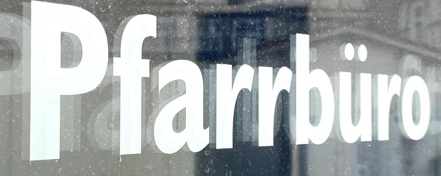 Schild mit Aufschrift 'Pfarrbüro' vor unscharfem Hintergrund