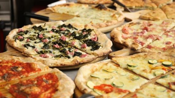 Das Foto zeigt mehrere verschiedene, bereits fertig gebackene Pizzen auf einem Tisch, im Hintergrund sieht man Teile der Ausstattung einer (professionellen) Küche