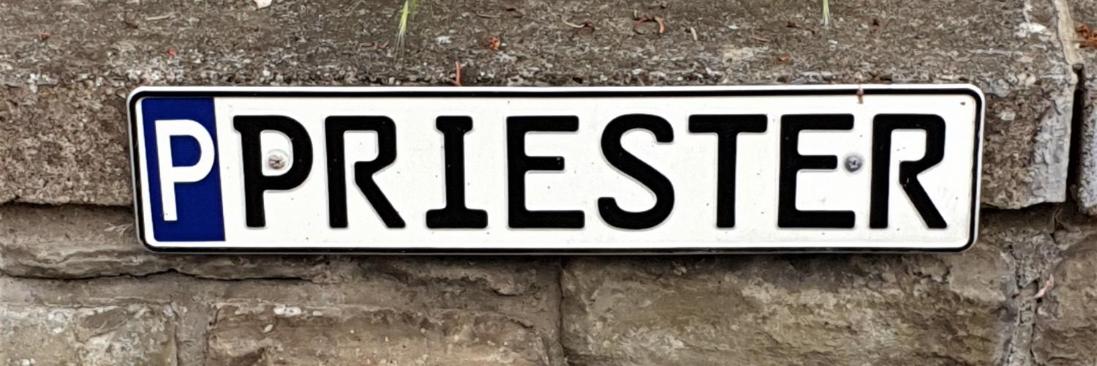Parkschild für Priester-Parkplatz, mit 'P' gekennzeichnetes Parkschild mit Aufschrift 'Priester', befestigt an einer Mauer