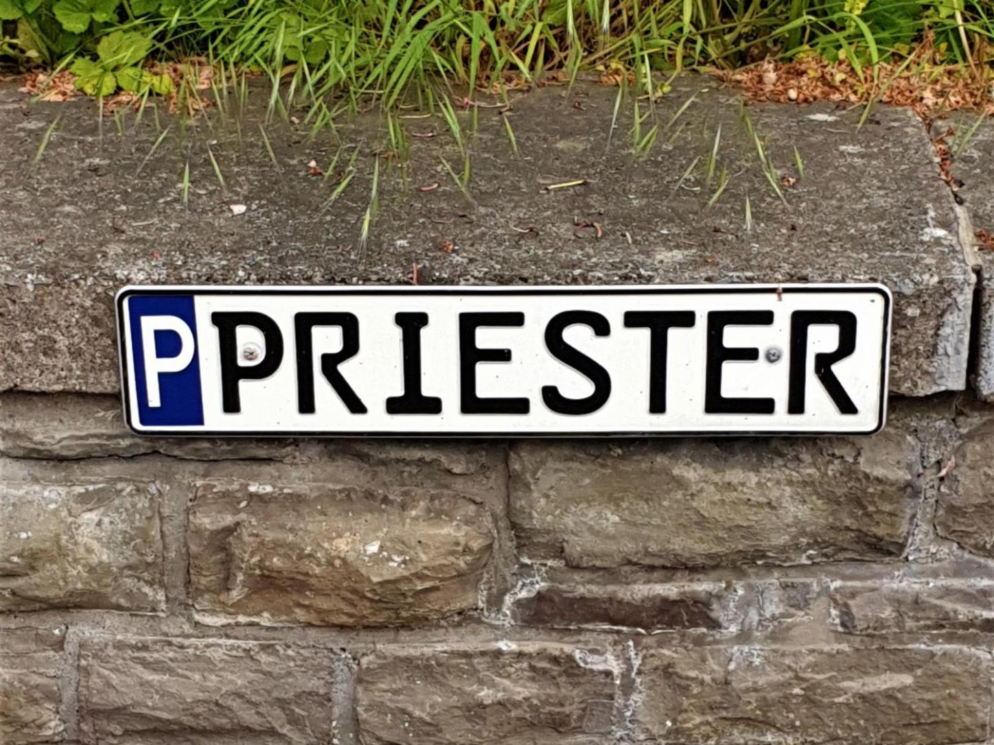 Parkschild für Priester-Parkplatz, mit 'P' gekennzeichnetes Parkschild mit Aufschrift 'Priester', befestigt an einer Mauer