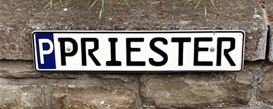 Parkschild für Priester-Parkplatz, mit 'P' gekennzeichnetes Parkschild mit Aufschrift 'Priester', befestigt an einer Mauer