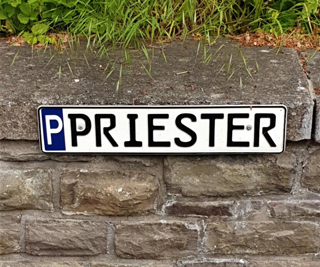 Parkschild für Priester-Parkplatz, mit 'P' gekennzeichnetes Parkschild mit Aufschrift 'Priester', befestigt an einer Mauer
