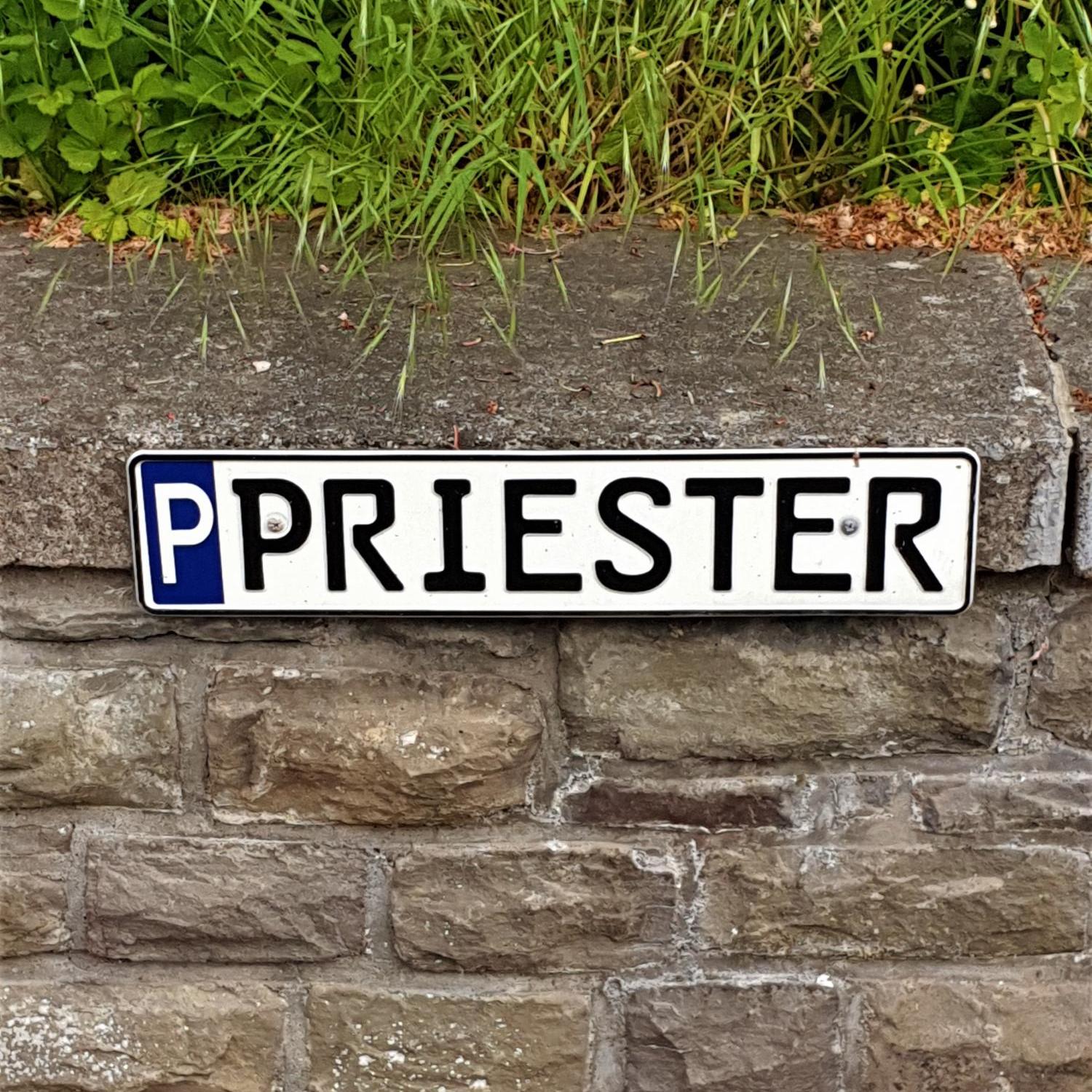 Parkschild für Priester-Parkplatz, mit 'P' gekennzeichnetes Parkschild mit Aufschrift 'Priester', befestigt an einer Mauer