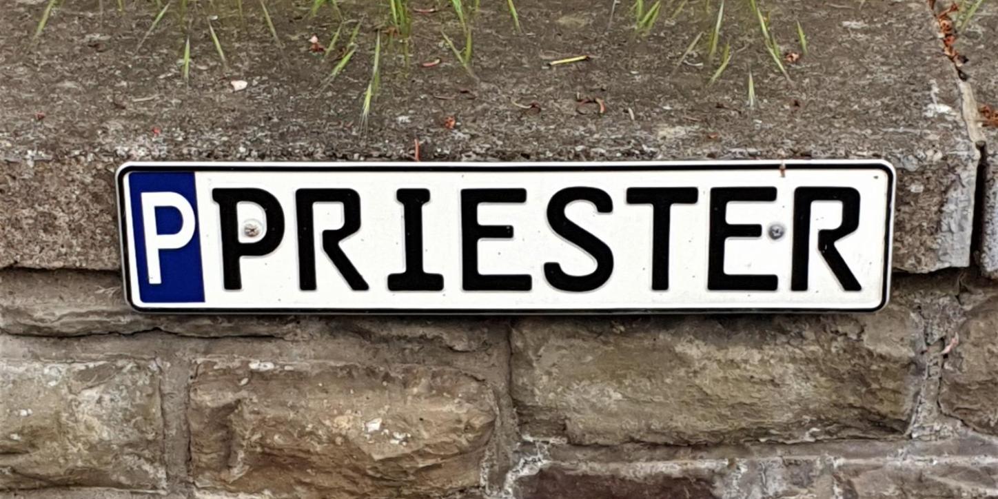 Parkschild für Priester-Parkplatz, mit 'P' gekennzeichnetes Parkschild mit Aufschrift 'Priester', befestigt an einer Mauer