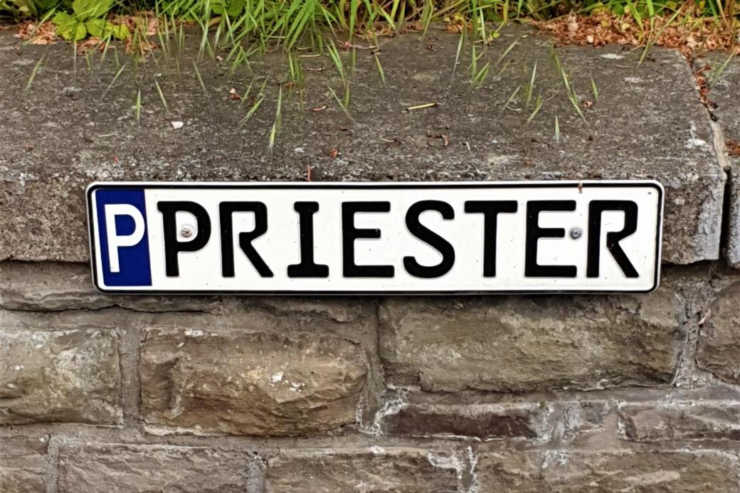 Parkschild für Priester-Parkplatz, mit 'P' gekennzeichnetes Parkschild mit Aufschrift 'Priester', befestigt an einer Mauer