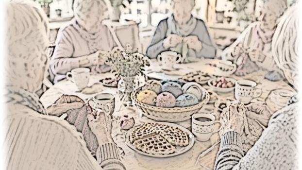 Strickende Seniorinnen sitzen an einem Tisch, auf dem Wollknäuel in einem Korb aber auch Kaffeetassen und Teller mit süßen Waffeln stehen