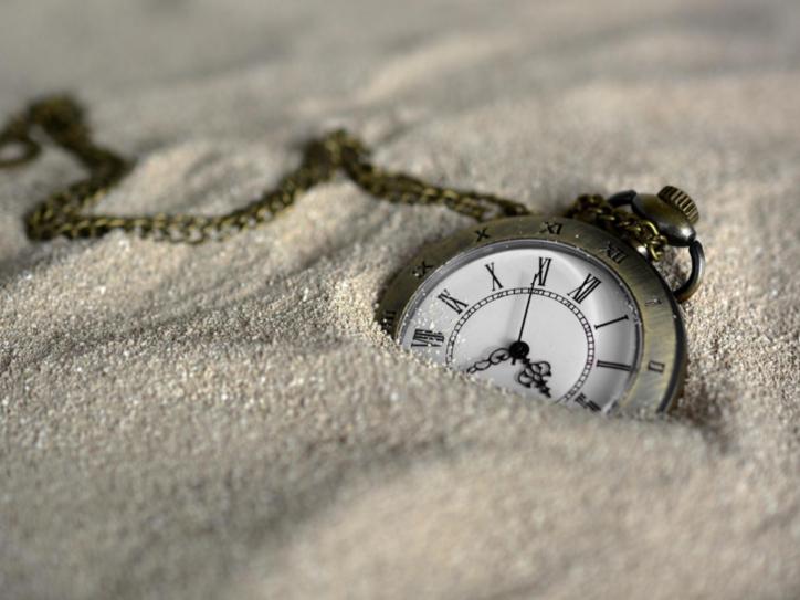Eine Taschenuhr mit klassischem Ziffernblatt und Kette, halb im Sand vergraben