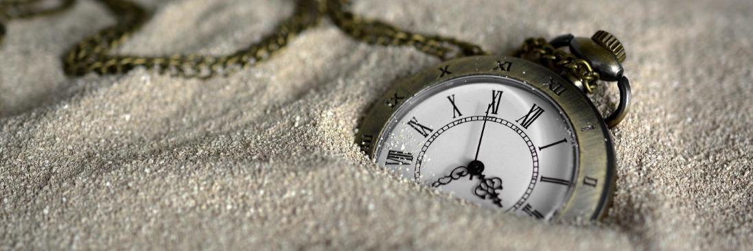 Eine Taschenuhr mit klassischem Ziffernblatt und Kette, halb im Sand vergraben