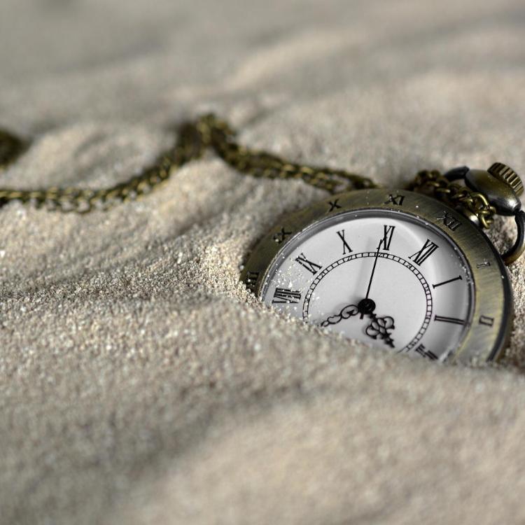 Eine Taschenuhr mit klassischem Ziffernblatt und Kette, halb im Sand vergraben