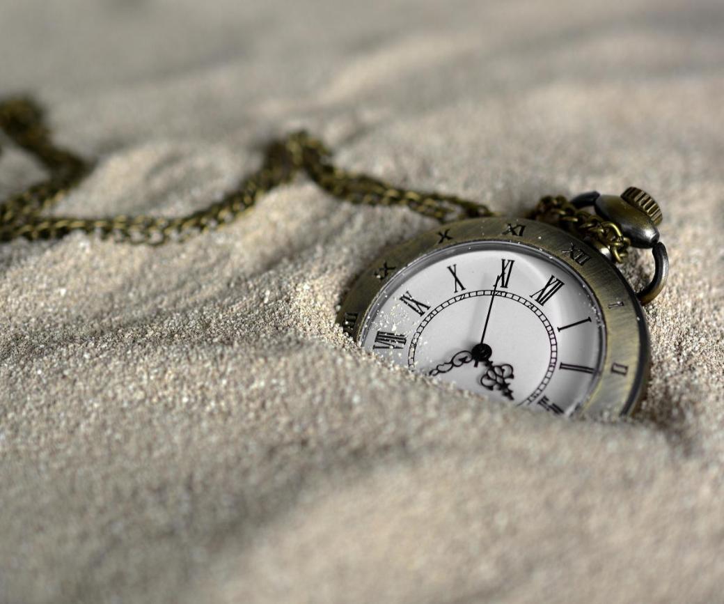 Eine Taschenuhr mit klassischem Ziffernblatt und Kette, halb im Sand vergraben