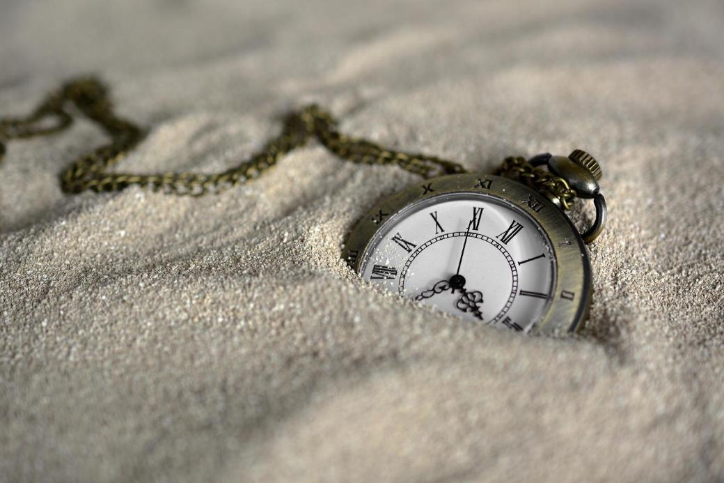 Eine Taschenuhr mit klassischem Ziffernblatt und Kette, halb im Sand vergraben