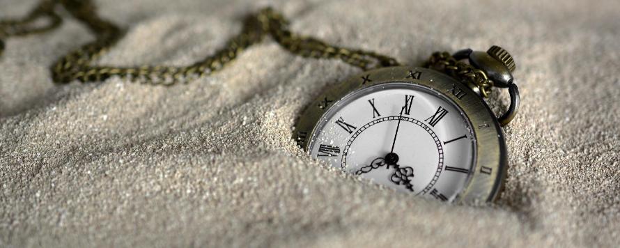 Eine Taschenuhr mit klassischem Ziffernblatt und Kette, halb im Sand vergraben