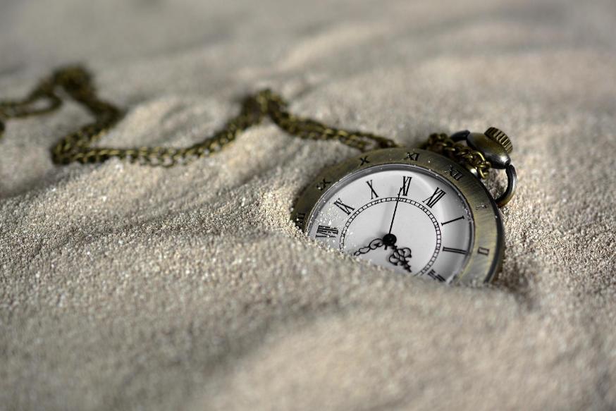 Eine Taschenuhr mit klassischem Ziffernblatt und Kette, halb im Sand vergraben