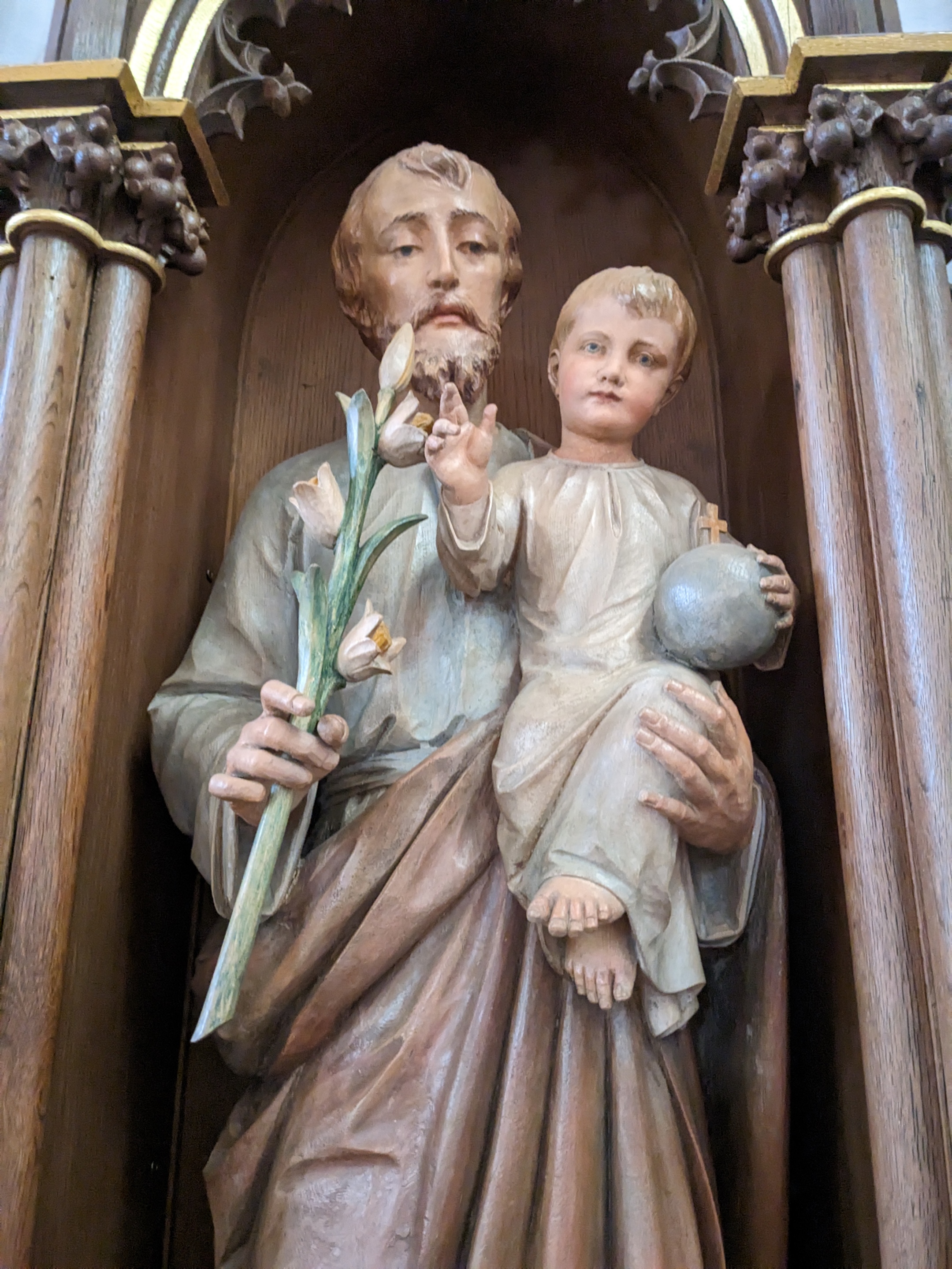 Nahaufnahme des Heiligen Josefs. In der Linken Hand hält er eine Lilie und in der rechten Hand hält er das Jesuskind. Das Jesuskind trägt in der rechten Hand die Weltkugel.