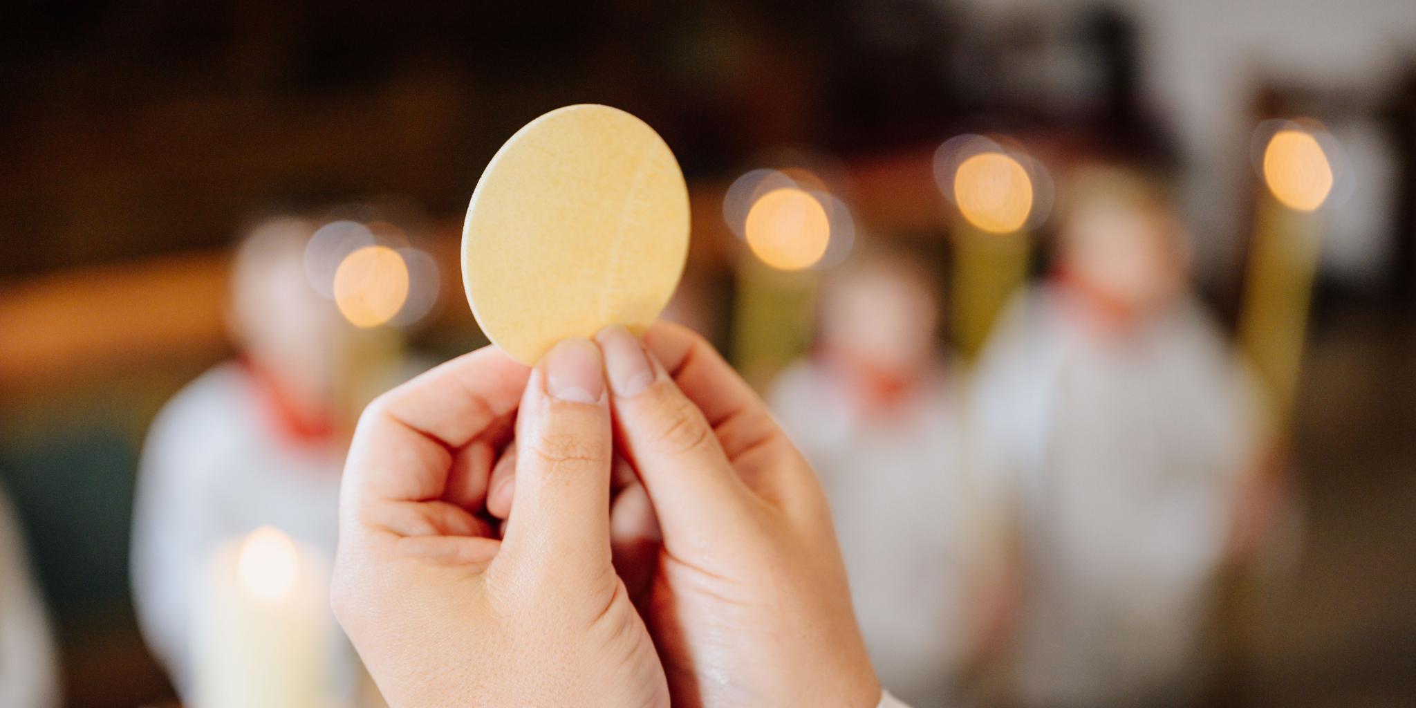 Ein Priester hält eine Hostie während der Eucharistiefeier hoch