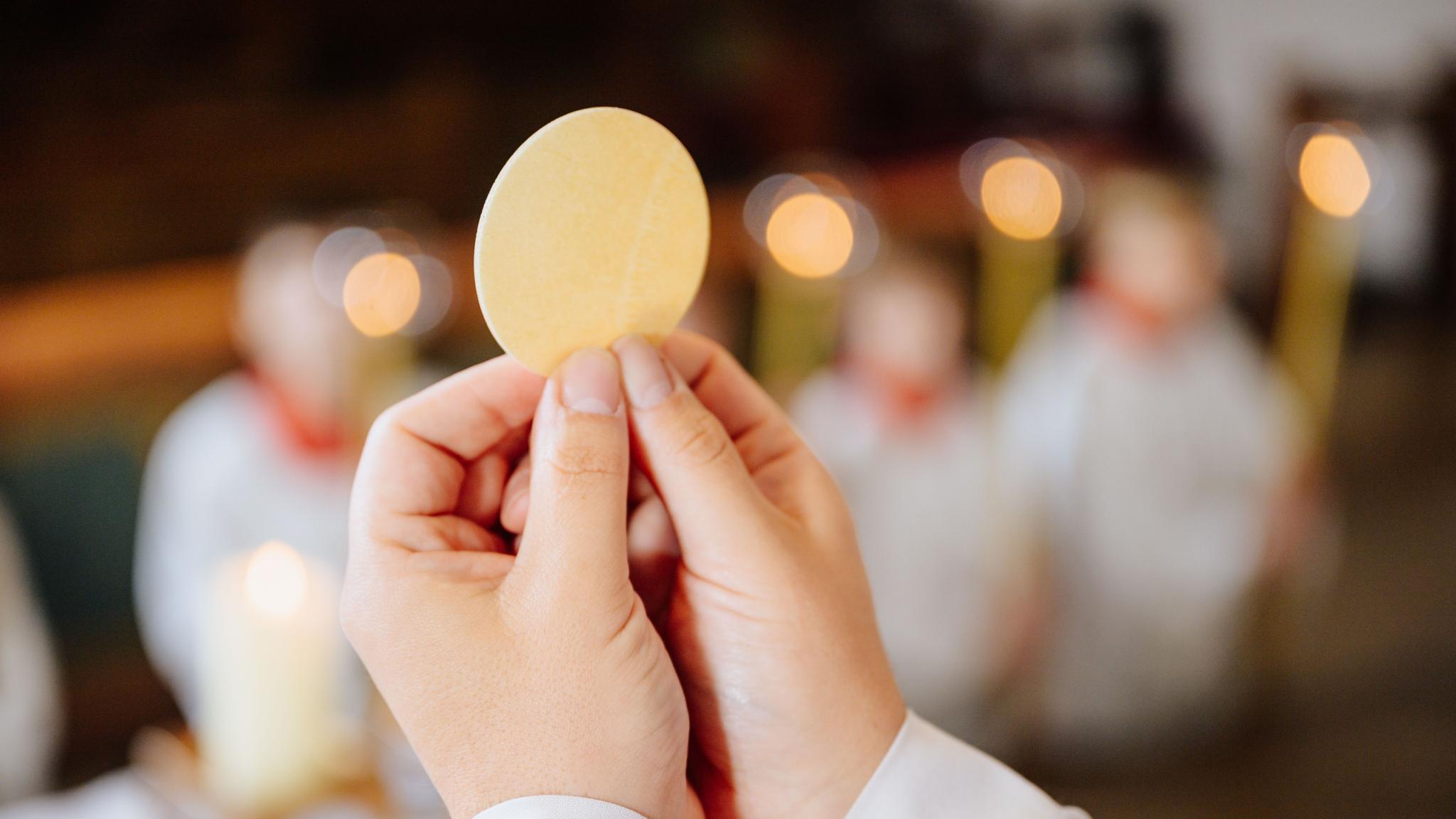 Ein Priester hält eine Hostie während der Eucharistiefeier hoch