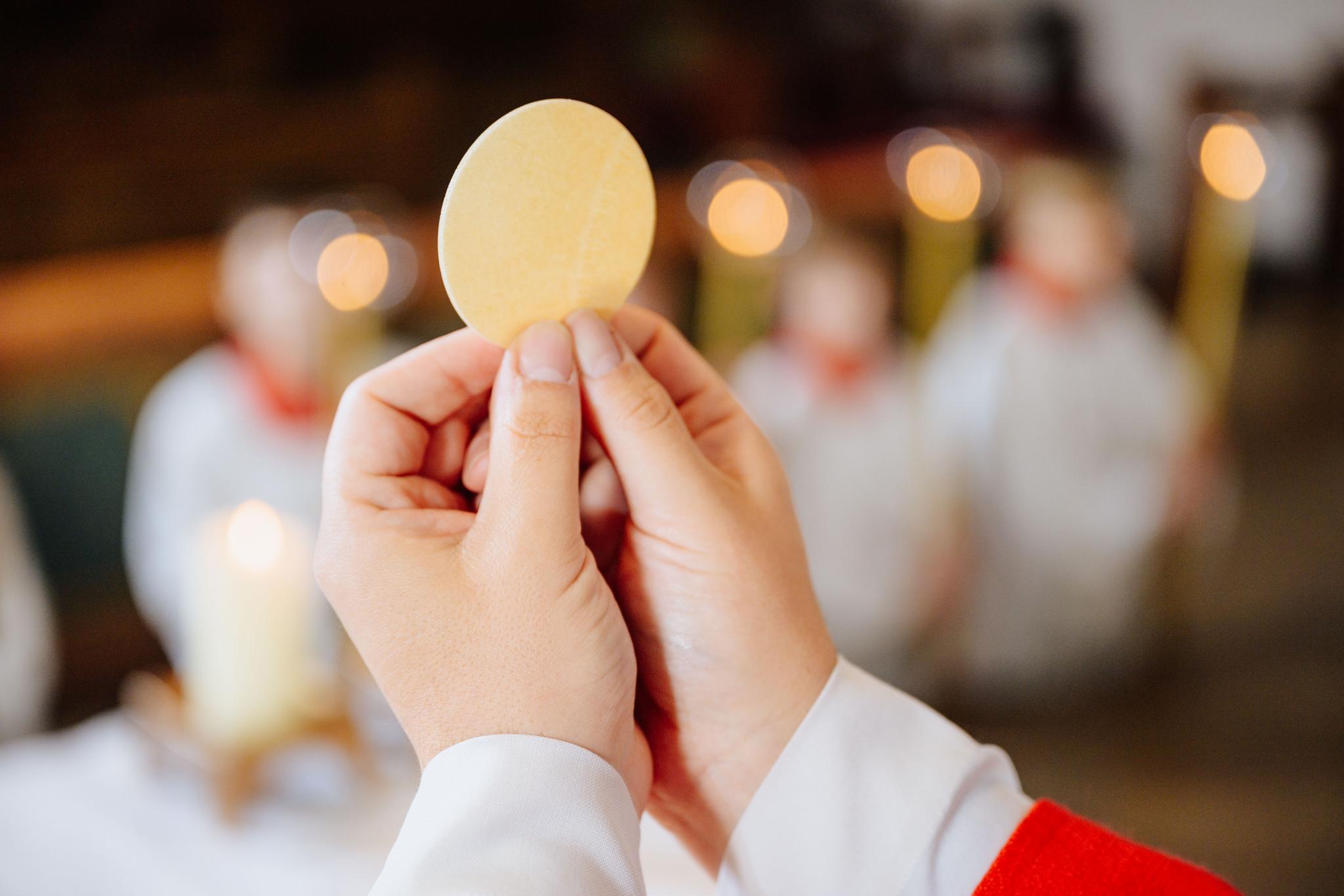 Ein Priester hält eine Hostie während der Eucharistiefeier hoch