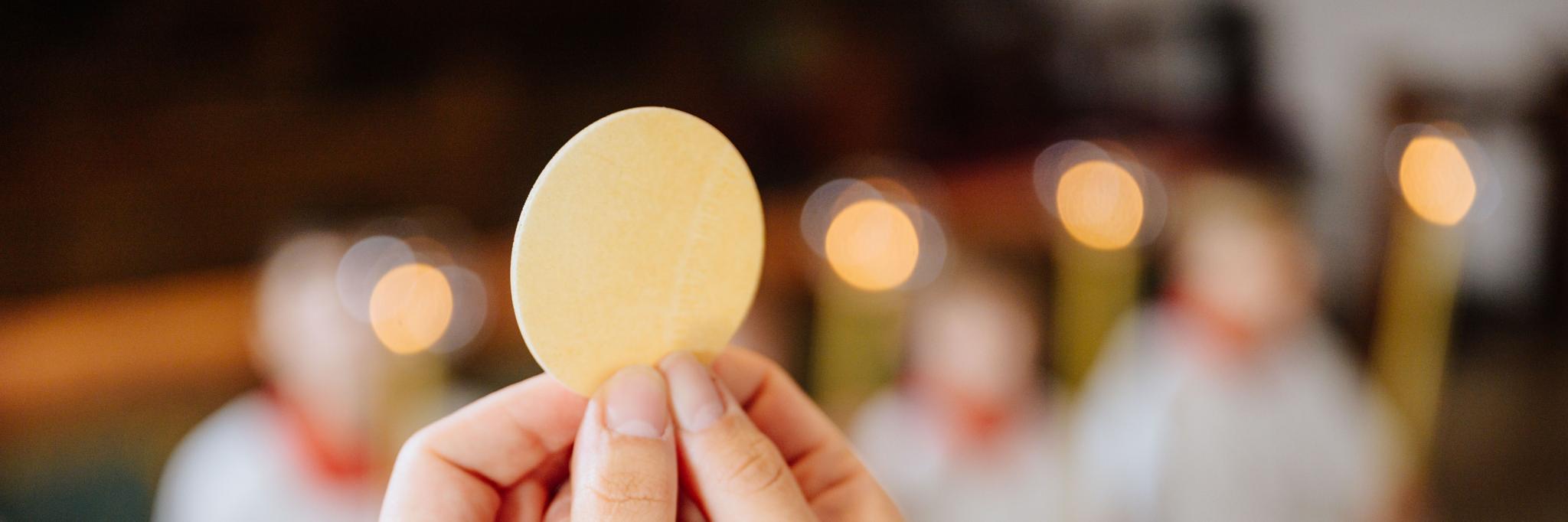 Ein Priester hält eine Hostie während der Eucharistiefeier hoch